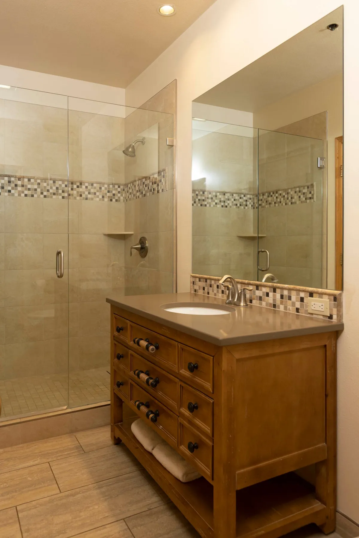 This image showcases a beautifully designed bathroom featuring a glass shower enclosure, a stylish wooden vanity, and a mirrored wall. The space is bathed in soft, inviting light, creating an atmosphere perfect for relaxation and rejuvenation after a long day on the slopes or outdoor adventures.