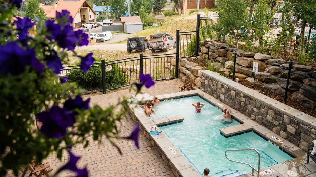 An inviting exterior shot of a hot tub surrounded by greenery, decorative flower pots, and a stone wall. The scene suggests a tranquil spot for relaxation and socializing, with room for multiple guests.