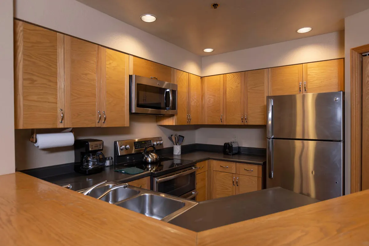 A cozy yet stylish kitchen scene showcasing stainless steel appliances, warm wood cabinetry, and polished granite countertops. Sunlight streams into the room, creating a comfortable space ideal for preparing meals and hosting intimate breakfasts or dinners.
