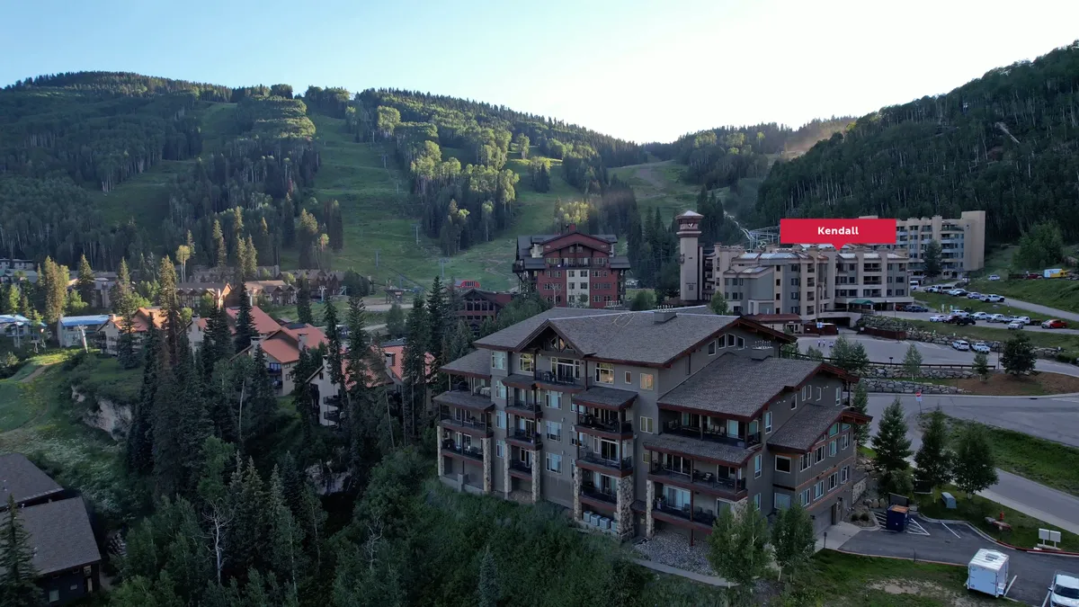 A wide view of the mountain landscape with residential buildings and a parking area, emphasizing easy access to outdoor activities like skiing and hiking, as well as community-centric events.