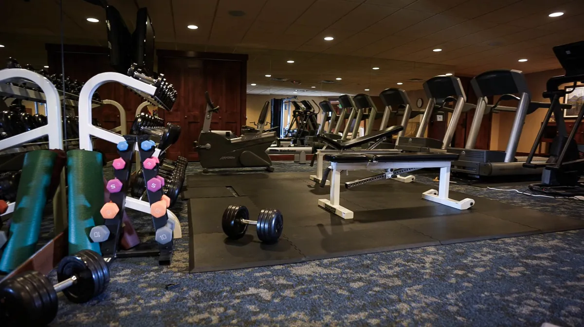This image showcases a well-equipped fitness center, featuring dumbbells, modern exercise machines, and a weight bench. The setting is bright, inviting, and geared toward promoting an active lifestyle, with ample space for cardio and strength training.