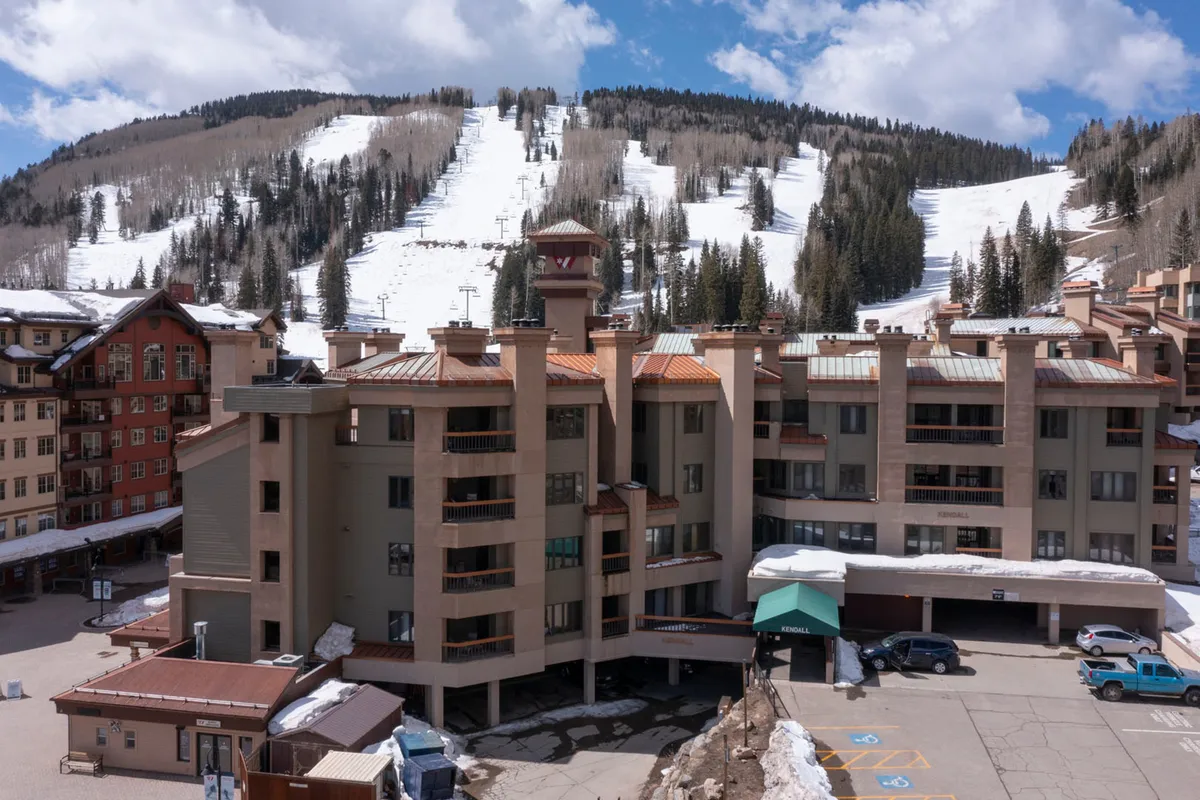 The building facade of a lodge is surrounded by a pristine, snow-covered landscape and dramatic mountain slopes. The scene conveys both a warm welcome and the adventurous spirit of the location, suggesting easy transitions from indoor comfort to outdoor fun.