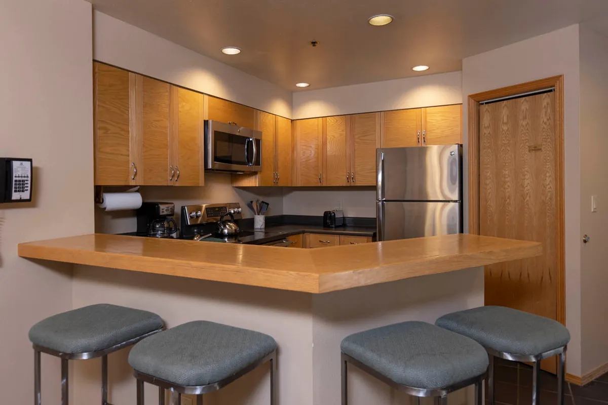 A bright, inviting kitchen featuring a spacious counter with stools, sleek stainless steel appliances, and an open layout ideal for both cooking and socializing. The area is set up to accommodate multiple people, evoking the sense of gathering and shared experiences.