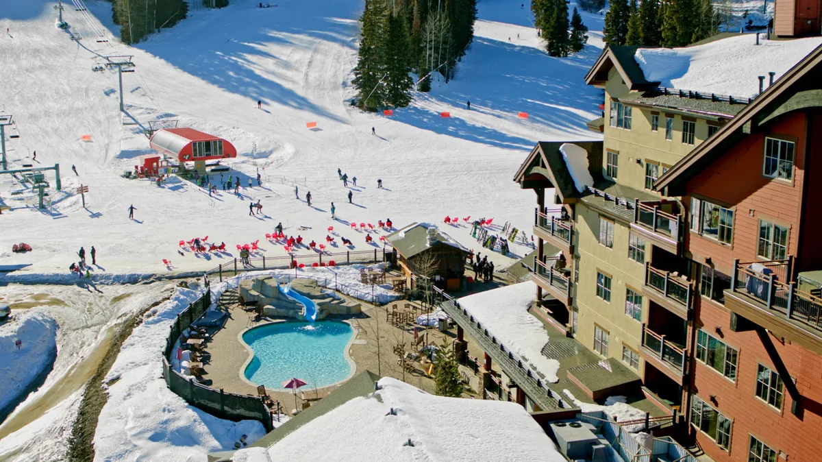 This image captures the exterior of a resort building featuring a swimming pool, hot tub, and ski slopes in the background. The pool and hot tub are key amenities framed by the picturesque mountain landscape, creating an inviting atmosphere that combines relaxation with alpine adventure.