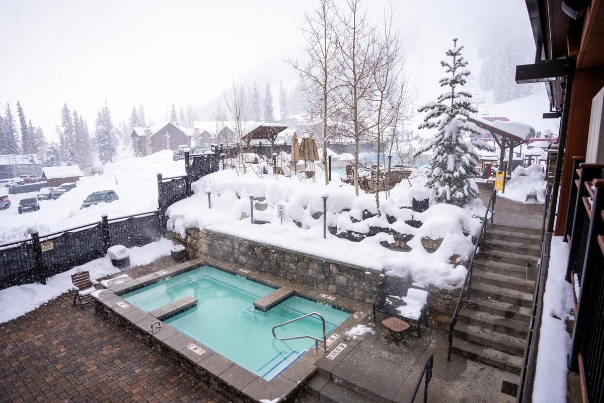 This interior-oriented exterior image features a hot tub surrounded by a snowy landscape and pine trees, with stone walls adding to the cozy ambiance. The inviting hot tub scene evokes feelings of relaxation, making it an ideal setting for unwinding and creating lasting memories with loved ones.